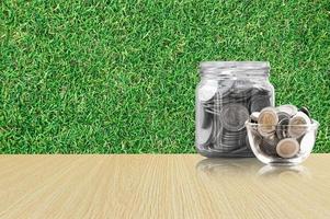 Münzen im ein Glas Krug auf Holz Fußboden ,Ersparnisse Münzen - - Investition und Interesse Konzept Speichern Geld Konzept, wachsend Geld auf Schweinchen Bank. isoliert auf Gras Hintergrund foto