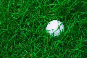 grünes gras mit golfball nahaufnahme im weichzeichner bei sonnenlicht. sportplatz für golfclubkonzept foto