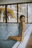 schöne junge Frau, die am Schwimmbad sitzt foto