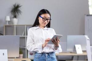 jung schön asiatisch Lehrer Arbeiten mit Tablette, im Klassenzimmer mit Computers foto