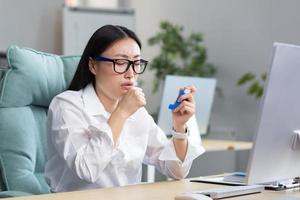 Allergie, Gefühl nicht wohl beim das Arbeitsplatz. ein jung asiatisch Frau Verwendet ein Inhalator im das Büro foto