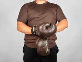 Junger Mann steht und zieht sich sehr alte braune Boxhandschuhe an foto