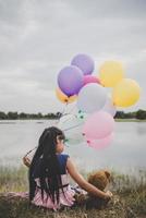 kleines Mädchen mit einem Teddybär und Luftballons auf Wiesenfeld foto