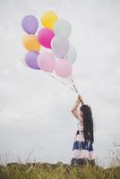 kleines Mädchen, das mit Luftballons auf Wiesenfeld spielt foto