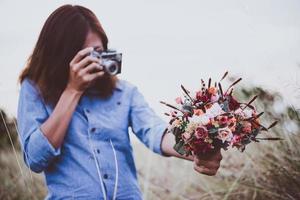 Nahaufnahme der Hand der jungen Hipsterfrau, die Retro-Kamera hält und Foto des roten Blumenstraußes schießt