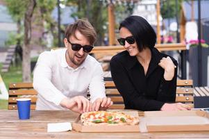 ein Kerl ist Sitzung mit ein Mädchen auf das Terrasse von ein Restaurant und reißt aus ein Pizza foto