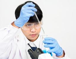 asiatisch männlich Schüler Wissenschaftler tragen ein Arzt Kleid im das Labor suchen beim das Chemiker. verursacht durch Mischen Reagenzien im wissenschaftlich Forschung Laboratorien mit Prüfung Röhren und Mikroskop auf das Tabelle foto