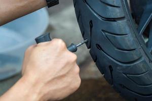 Der Fahrer verwendet ein Reifenstopfen-Kit und versucht, ein Loch in der Seitenwand des Reifens zu reparieren, einen platten Motorradreifen in der Garage zu reparieren. motorradwartungs- und reparaturkonzept foto