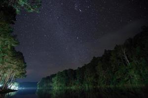 Sternenhimmel über Wasser und Bäume in der Nacht foto