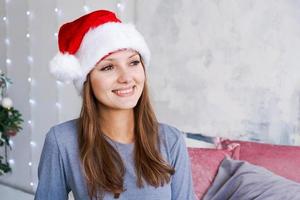 ein emotional Mädchen im Santa claus Hut und Blau Pyjama sitzt im Morgen auf Bett foto