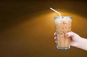 Frau Hand halten das Glas vereist Kaffee auf braun grungy Mauer Hintergrund foto