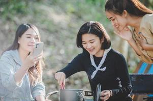 junge Frauen, die kochen und Smartphones benutzen, fotografieren beim Camping foto