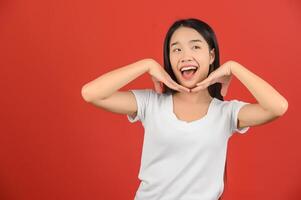 Porträt von glücklich jung asiatisch Frau im Weiß T-Shirt lächelnd Kinn auf Hand isoliert auf rot Hintergrund foto