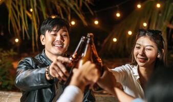 porträt glücklicher asiatischer freunde, die zusammen eine dinnerparty haben - junge leute sitzen am bartisch und toasten biergläser abendessen im freien - leute, essen, trinken lebensstil, neujahrsfeierkonzept. foto