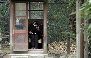 Nagoya, Japan - - Januar 3, 2013 - - ein bewachen tragen ein Gesicht Maske sitzt im ein hölzern Hütte im ein Park während haben ein Telefon Gespräch. foto