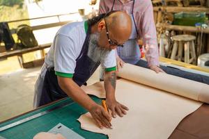 asiatisch Mann Leder Handwerker ist mit ein Cutter Messer zu Schnitt ein Stück von Weiß Leder groß Blatt gemäß zu das Design zu bringen aus zu nähen in Produkte zum Kunden. foto
