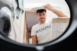 Mann mit Korb, Aussicht von Waschen Maschine innen. männlich tut Wäsche Täglich Routine. foto
