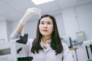 junge medizinische wissenschaftlerin, die reagenzglas im medizinischen labor betrachtet foto