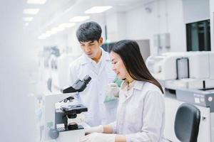 Zwei medizinische Wissenschaftler, die im medizinischen Labor arbeiten, junge Wissenschaftlerin, die sich das Mikroskop ansieht. Fokus auf junge Wissenschaftlerinnen wählen foto