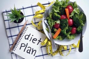 Konzept für gesunde Ernährung. Gemüsesalat, Notizbuch zur Lebensmittelkontrolle und Maßband foto