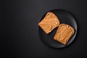 nahrhaft Sandwich bestehend aus von Brot und Erdnuss Butter auf ein schwarz Keramik Teller foto