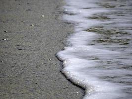 Meereswellenschaum am Sandstrandufer foto