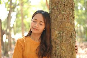 Konzept von Speichern das Welt asiatisch Frau halten ein Baum mit ihr Augen geschlossen zu Erfahrung das Leistung von Natur foto