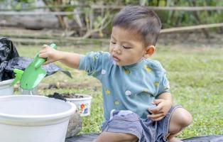 kleines kind schaufelt erde in töpfe, um pflanzen zum pflanzen vorzubereiten. kleinkindjunge, der erde zum pflanzen für den kleinen helfer der mutter gräbt. Gartenarbeit. hobbys zu hause gartenbau. freizeitkonzept foto