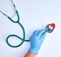 Mensch Hand im Blau steril Handschuhe halten ein Grün Stethoskop foto
