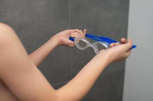 ein Kind hält Schwimmen Brille im seine Hände foto