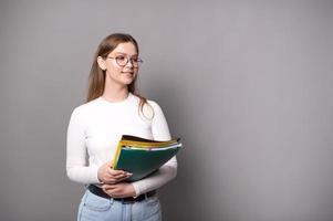 süß Schüler mit Brille hält bunt Ordner auf ein grau Hintergrund foto