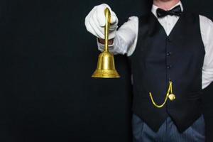Porträt von Butler oder Kellner mit goldener Servierglocke. konzept des ringes für den service. professionelle Gastfreundschaft und Höflichkeit. foto
