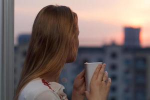 Frau trinkt Tee und beobachtet einen Sonnenuntergang