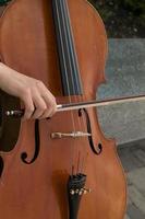 Detail von ein Mann spielen das hölzern Cello Reiben das Saiten mit das Bogen zu erhalten das Anmerkungen von ein klassisch Musik- Stück. foto