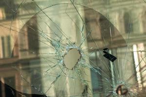 ein Loch im das Fenster Glas mit ein Kugel während ein Militär- Schießen. Risse verbreiten um das Loch. schmutzig Fenster rahmen. Aussicht von das Straße von das innen. foto