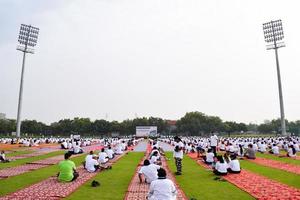 neu-delhi, indien, 21. juni 2022 - gruppen-yoga-übungssitzung für menschen im yamuna-sportkomplex in delhi am internationalen yoga-tag, große gruppe von erwachsenen, die an yoga-kursen im cricket-stadion teilnehmen foto