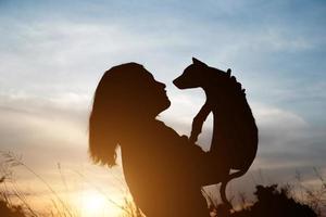 Schattenbild der Frau, die kleinen Hund am Sonnenuntergangsfeld hält foto