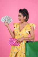 junge modische Frau, die eine Brieftasche mit Bargeld und Einkaufstüten hält foto