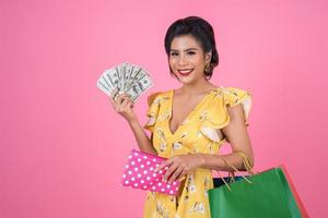 junge modische Frau, die eine Brieftasche mit Bargeld und Einkaufstüten hält foto