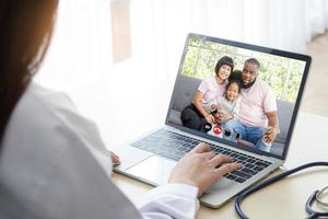 ein Frau Arzt chatten Über ein online Video Anruf mit ein Afroamerikaner Familie von Patienten. Konzept von kommunizieren durch Technologie online. Ärzte können untersuchen Patienten durch Video Anrufe. foto