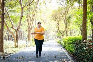 Fett asiatisch Frau tragen Gelb Bluse Joggen im das Morgen im das Park. Konzept von Gewicht Verlust Übung zum das gut Gesundheit von fettleibig Personen. Kopieren Raum foto