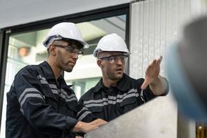 zwei vielfältig Fachmann schwer Industrie Ingenieure tragen Sicherheit Uniform und schwer Hüte Arbeiten Industrie und Ingenieurwesen Menschen Technologie Konzept . foto