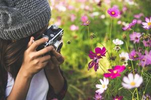 Hipster-Mädchen mit Vintage-Kamera-Fokus, der Blumen in einem Garten schießt foto