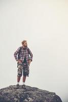 junger Hipster-Wanderer mit Rucksack, der oben auf dem Berg sitzt
