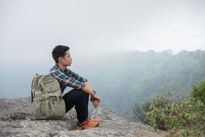 junger Hipster-Wanderer mit Rucksack, der oben auf dem Berg sitzt