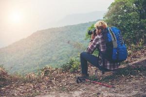 Rückseite des jungen Reisenden mit Rucksack, der auf Berg steht und ein Foto macht