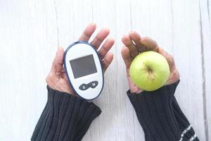 ältere Frau, die diabetische Messwerkzeuge und Apfel auf Holztisch hält foto