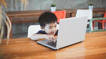 vier Jahr alt Junge asiatisch Mann sitzt beim ein Bildschirm während studieren beim ein Kaffee Geschäft mit seine Laptop zu Studie online während das covid-19 Abriegelung. online Ausbildung, Schule zu Hause. foto