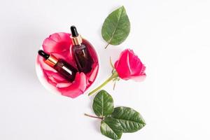 zwei kosmetisch Flaschen mit ein Gold Deckel und ein Pipette mit natürlich Rose Öl oder feuchtigkeitsspendend Serum zum Selbstpflege Lüge im ein Schüssel mit Rose Blütenblätter. oben Sicht. foto