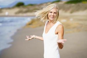 glückliche reife frau, die am strand spaziert, ihre freizeit verbringt, ihre freizeit genießt foto